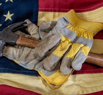 Workman's gloves and a hammer sitting atop the U.S. flag symbolizing American blue-collar workers.