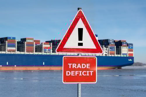 A container ship representing the import and export of goods with a warning sign with the text `Trade deficit` on the shore.
