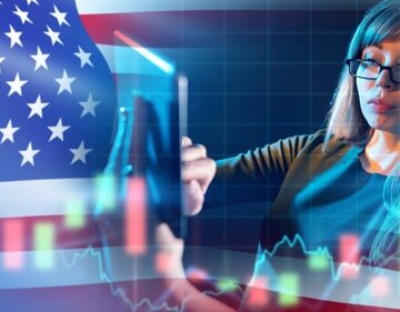 A businesswoman using a tablet to analyze financial trading charts overlaid with the American flag.