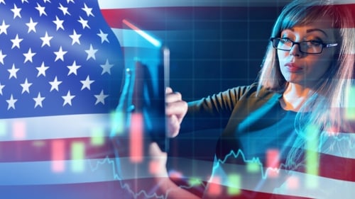 A businesswoman using a tablet to analyze financial trading charts overlaid with the American flag.