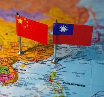 A map of East and Southeast Asia with two small flags pinned onto it, the left flag pinned over mainland China, and the right flag pinned over the island of Taiwan.