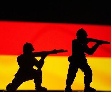 Silhouettes of soldiers in combat positions against the backdrop of the German national flag.