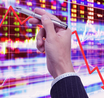Stock,Market,Crash A man's hand pointing with a pen to a stock market chart featuring a red trend line pointing downward, commonly used to represent market declines.