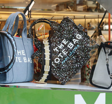 A lineup of Marc Jacobs "The Tote Bag" handbags in various materials and patterns.
