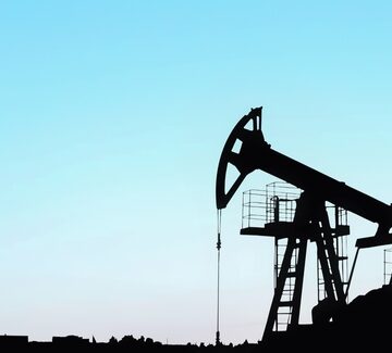 The silhouette of a crude oil pumpjack against a blue evening sky.