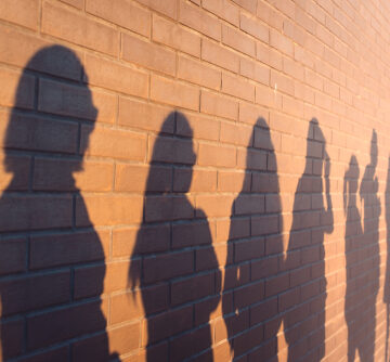 A,Line,Of,Shadows,Of,People,Lined,Up,Against,A A line of shadows of voters waiting in line, projected onto a brick wall.