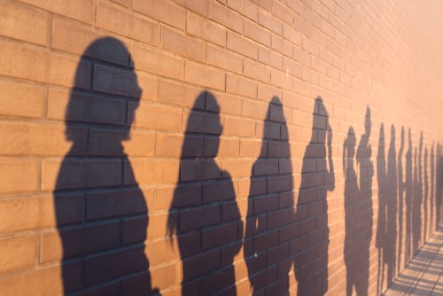 A,Line,Of,Shadows,Of,People,Lined,Up,Against,A A line of shadows of voters waiting in line, projected onto a brick wall.