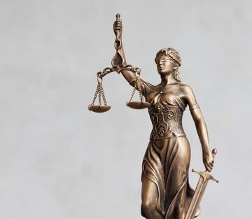 An image of Lady Justice (or Themis), a widely recognized symbol of the legal system holding scales of justice in one hand, a sword in the other hand, and wearing a blindfold.