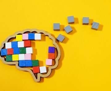 A brain shape made of colorful blocks representing the complexity of thought and memory with gray pieces falling away symbolizing cognitive impairment.