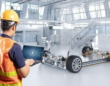 An engineer or technician using a laptop to monitor or configure the chassis of an electric vehicle platform that houses the battery pack, motors, and suspension system in a single unit.