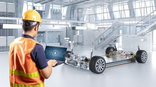 An engineer or technician using a laptop to monitor or configure the chassis of an electric vehicle platform that houses the battery pack, motors, and suspension system in a single unit.