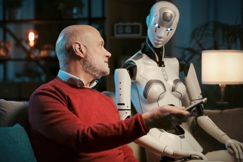 Senior,Man,And,Female,Android,Robot,Watching,Tv,Together,At A conceptual scenario of human-robot companionship, specifically showing a senior man interacting with a female humanoid robot on a couch.