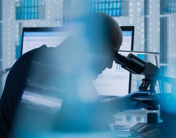 Male,Researcher,Or,A,Doctor,Examining,Medical,Research,Samples,Under A blurred image of scientist using a microscope in a laboratory setting.