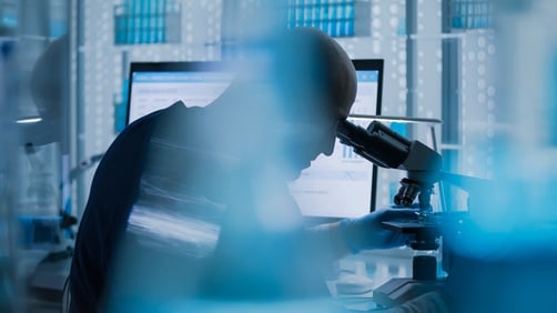 Male,Researcher,Or,A,Doctor,Examining,Medical,Research,Samples,Under A blurred image of scientist using a microscope in a laboratory setting.