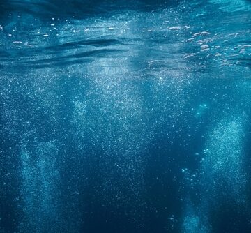 Underwater air bubbles rise to the surface in a deep blue sea.