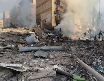 Photo shows the aftermath of devastating Israeli airstrikes in Beirut, Lebanon, specifically targeting residential buildings and infrastructure, showing emergency teams working through rubble while smoke billows from heavily damaged high-rise structures.
