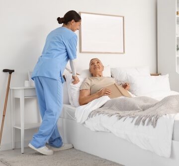 A female caregiver assisting a senior in a bedroom setting.