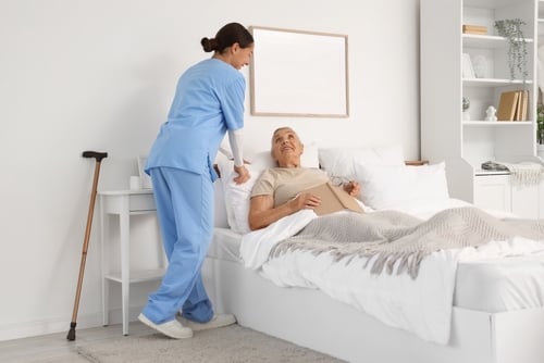 Female,Caregiver,Adjusting,Happy,Senior,Woman's,Pillow,In,Bedroom A female caregiver assisting a senior in a bedroom setting.