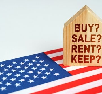 Real,Estate,Concept.,On,The,Us,Flag,Is,A,Model A U.S. flag under a small wooden house printed with the words "buy, sell, rent, or keep."