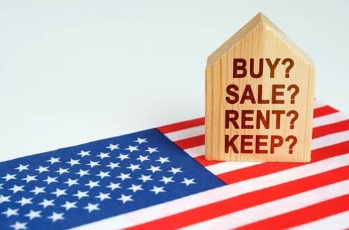 Real,Estate,Concept.,On,The,Us,Flag,Is,A,Model A U.S. flag under a small wooden house printed with the words "buy, sell, rent, or keep."