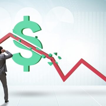 A distressed businessman looking at a sharp red arrow crashing downward through a large green dollar sign.
