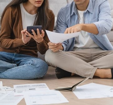 Family,Financial,Concept,,Stressed,Wife,And,Husband,Have,A,Problem A couple sit cross-legged on the livingroom floor reviewing financial documents together, suggesting a focus on budget management.