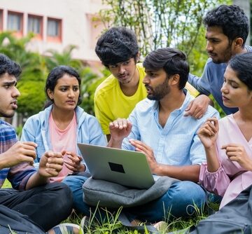 Group,Of,College,Students,Discussing,About,Project,With,Team,Leader A group of Indian students discussing a project on a laptop in a college campus.