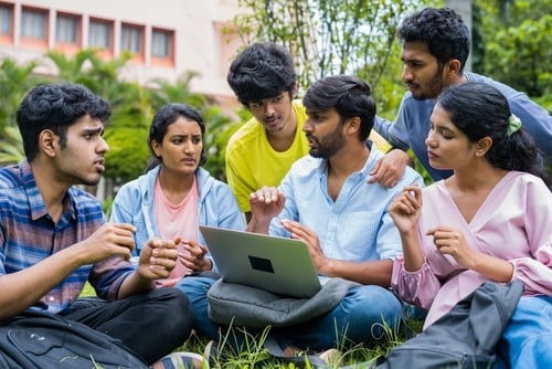 Group,Of,College,Students,Discussing,About,Project,With,Team,Leader A group of Indian students discussing a project on a laptop in a college campus.