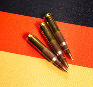 Three,Rifle,Cartridges,On,The,Flag,Of,Germany.,Close-up,,Copy Three rifle cartridges placed on top of a background featuring the flag of Germany.