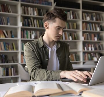 Remote,Learning.,Busy,Young,College,Student,Work,At,Library,Table A Gen Z-aged person focused on studying with a laptop in a library setting.