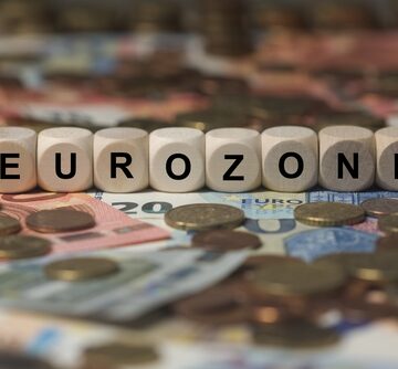 Eurozone,-,Cube,With,Letters,,Money,Sector,Terms,-,Sign White wooden cubes spelling "EUROZONE" placed on top of various Euro banknotes and coins.