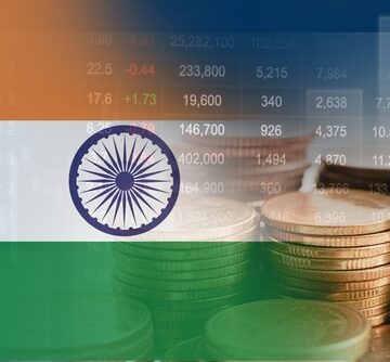 The national flag of India overlaid with a trading chart and stacks of coins. The national flag of India overlaid with a trading chart and stacks of coins.