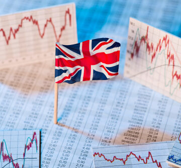A United Kingdom stock market and national economy concept depicting the Union Jack flag standing amid various printed financial spreadsheets, numerical data sheets, and volatile performance line graphs. A United Kingdom stock market and national economy concept depicting the Union Jack flag standing amid various printed financial spreadsheets, numerical data sheets, and volatile performance line graphs.
