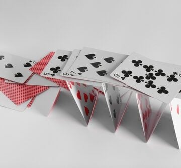 Collapsed,House,Of,Playing,Cards,On,Light,Grey,Background A delicate house of cards, built from standard playing cards, starting to collapse.