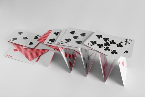 A delicate house of cards, built from standard playing cards, starting to collapse.