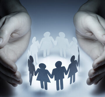 Two large hands cupping and protecting a paper-cutout circle of people holding hands, which is a classic visual metaphor for community. FINDING SECURITY IN AN INSECURE WORLD (Part I) – Overcoming Self-Deception and Self-Delusion