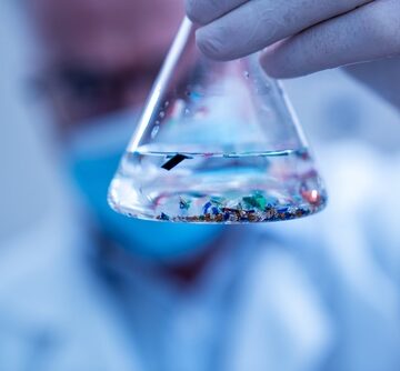 Scientist,Examining,Small,Plastic,Particles,Suspended,In,Water,In,A A scientist in a laboratory holds an Erlenmeyer flask containing water mixed with various small, colorful microplastic particles.