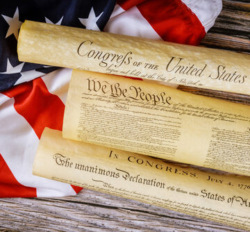 Closeup of artistic reproductions of key U.S. founding documents, including the Declaration of Independence and the Constitution next to the U.S. flag.