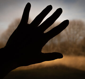 A silhouette of a human hand pressed against a window blocking the view of nature. A silhouette of a human hand pressed against a window blocking the view of nature.