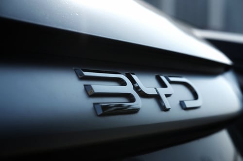 Close-up of the prominent, dark-finished logo of BYD, a major Chinese manufacturer of electric and plug-in hybrid vehicles. Close-up of the prominent, dark-finished logo of BYD, a major Chinese manufacturer of electric and plug-in hybrid vehicles.