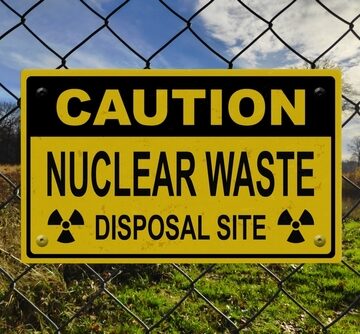 Black,And,Yellow,Caution,Sign,On,A,Fence,With,The A yellow and black radiation trefoil symbol on a caution sign indicating a nuclear waste disposal site located behind a chain-link fence.