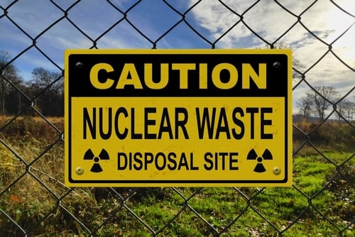 A yellow and black radiation trefoil symbol on a caution sign indicating a nuclear waste disposal site located behind a chain-link fence.