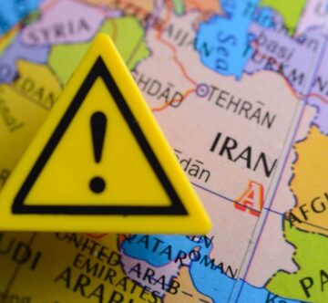 Close,Up,View,Of,Of,Iran,Country,At,The,Map Close-up view of a yellow warning triangle featuring an exclamation mark placed directly over Iran on a political map.