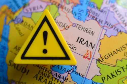 Close-up view of a yellow warning triangle featuring an exclamation mark placed directly over Iran on a political map.