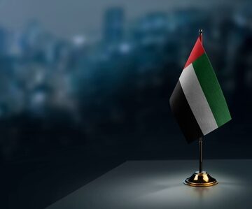 Small,Flags,Of,The,Arab,Emirates,On,An,Abstract,Blurry A miniature United Arab Emirates table flag, often used for office desk decorations or diplomatic settings.