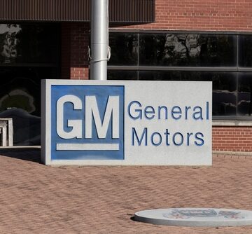 The General Motors (GM) logo on a sign outside a brick building.