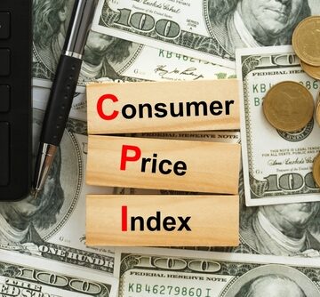 U.S. dollars and coins strewn across a table topped with a calculator and three blocks labeled Consumer", "Price", and "Index". U.S. dollars and coins strewn across a table topped with a calculator and three blocks labeled Consumer", "Price", and "Index".