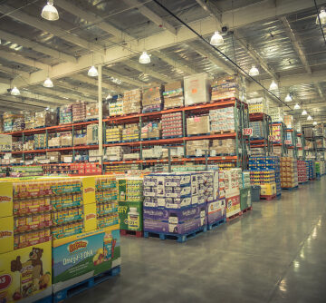 The interior of a Costco Wholesale warehouse showing high-ceiling aisles stocked with products on metal pallet racking. The interior of a Costco Wholesale warehouse showing high-ceiling aisles stocked with products on metal pallet racking.