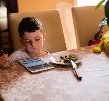 A little boy interacting with a tablet device while eating his meal.