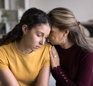 A motherly figure offering comfort and support to a downcast Gen-Z-aged woman.
